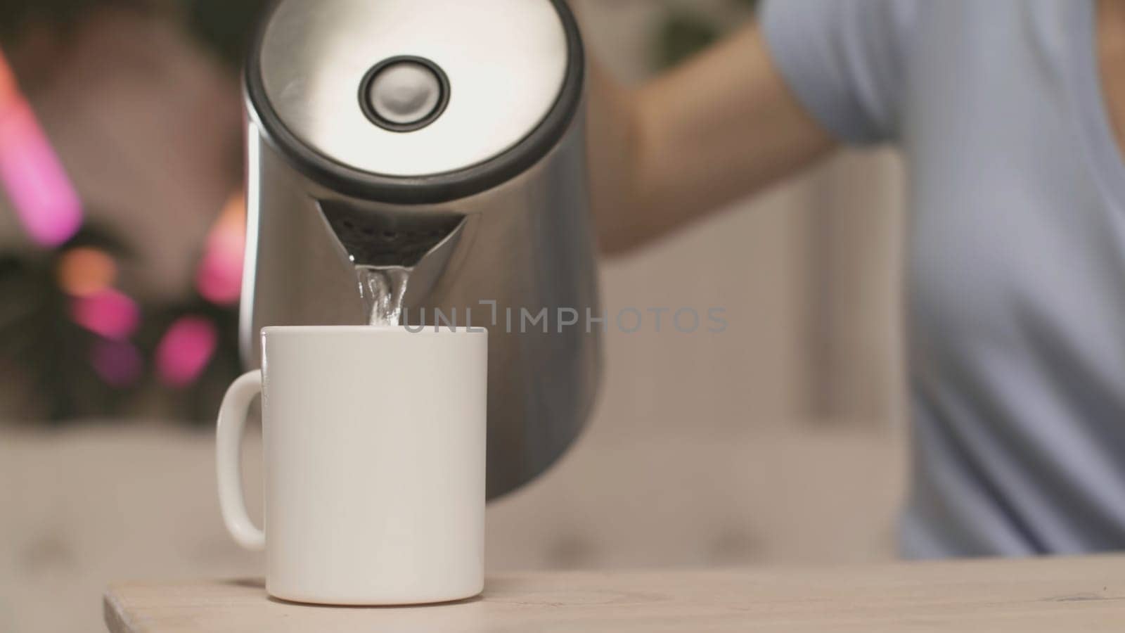 Close-up of women's hands pouring tea on background of lights. Stock footage. Young woman makes herself cup of tea. Woman makes tea on background of blurred lights.