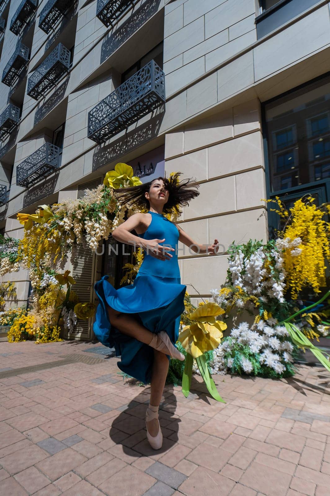 Beautiful Asian ballerina dances against the background of a building decorated with flowers. Vertical photo. by mrwed54