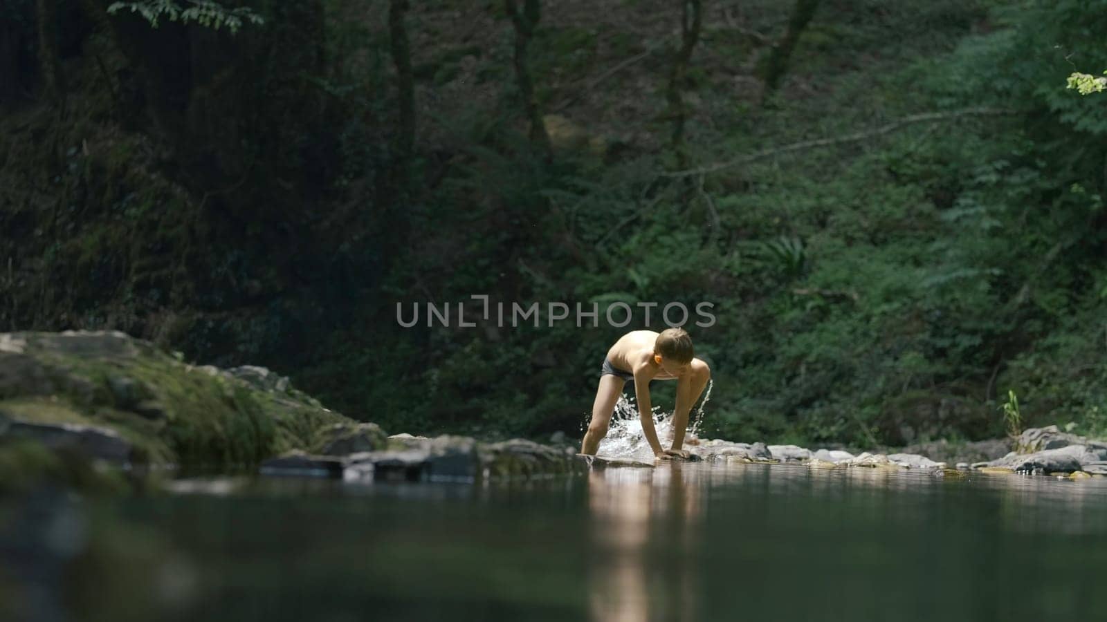 Boy swims in cold natural pond. Creative. Boy dives into natural pond in forest. Boy swims in lake in green forest by Mediawhalestock