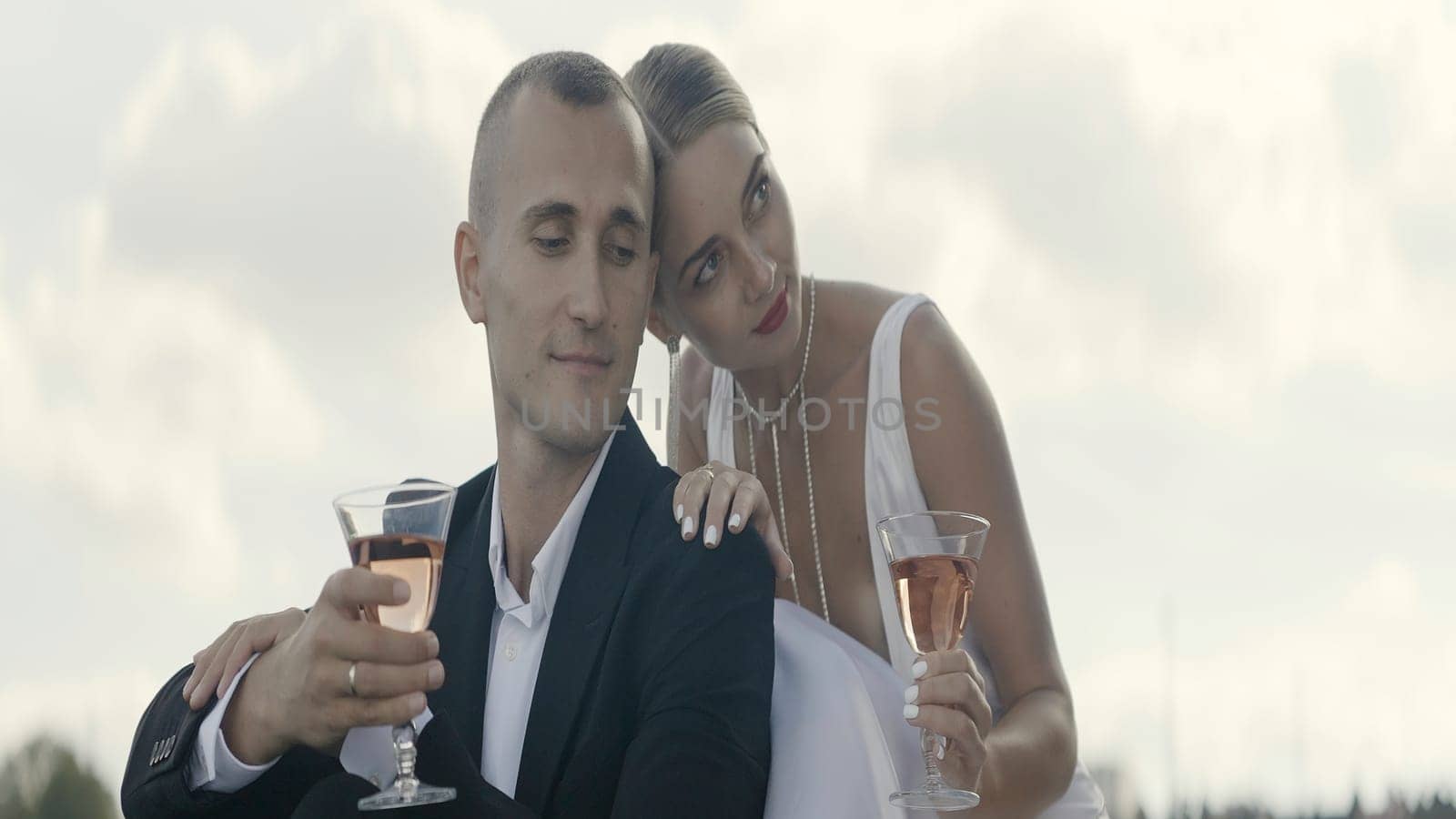 A dreaming couple. Action. A beautiful woman with her hair pulled back and a man who are hugging and drinking champagne from glasses. by Mediawhalestock