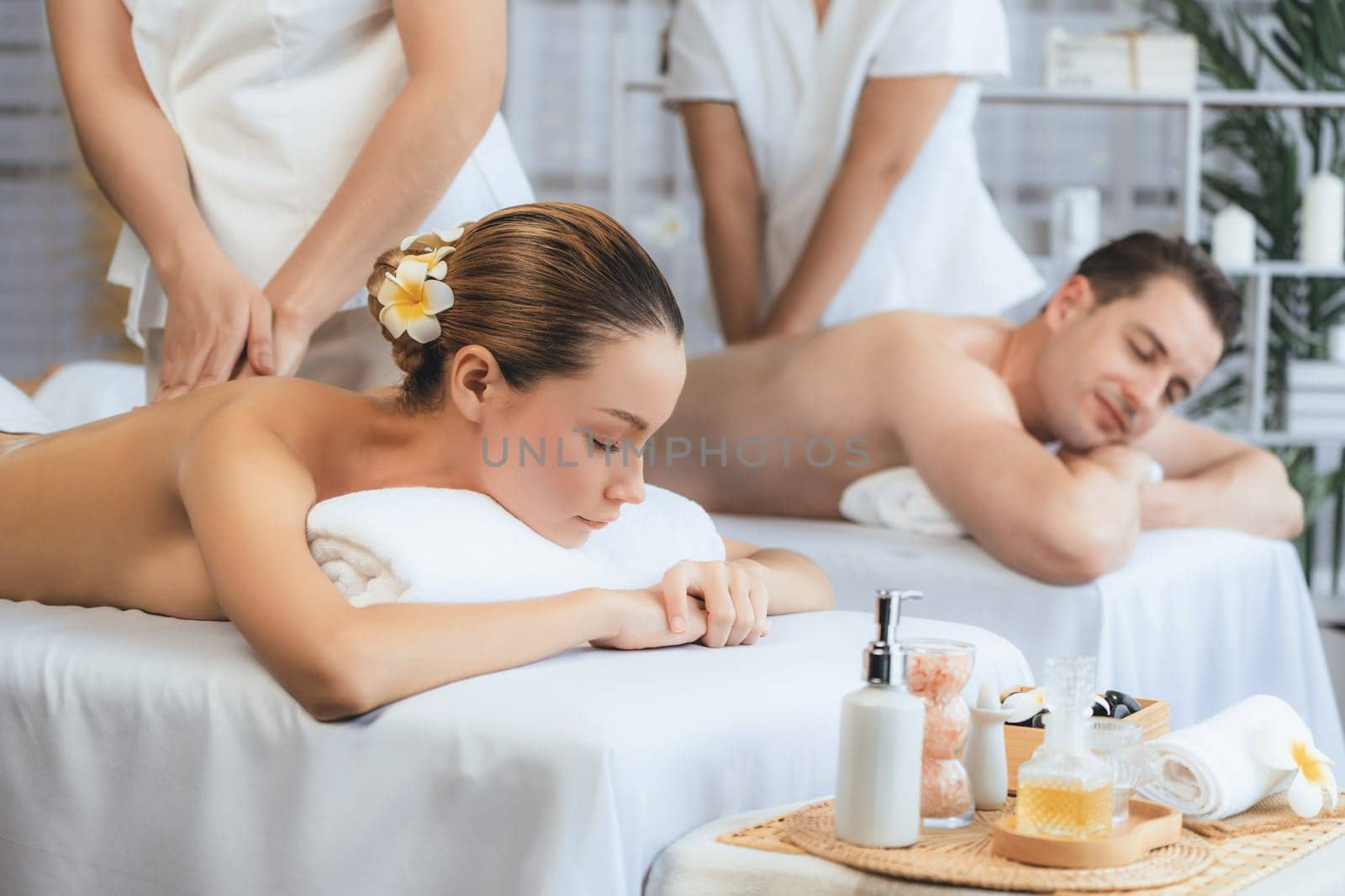 Caucasian couple customer enjoying relaxing anti-stress spa massage and pampering with beauty skin recreation leisure in day light ambient salon spa at luxury resort or hotel. Quiescent