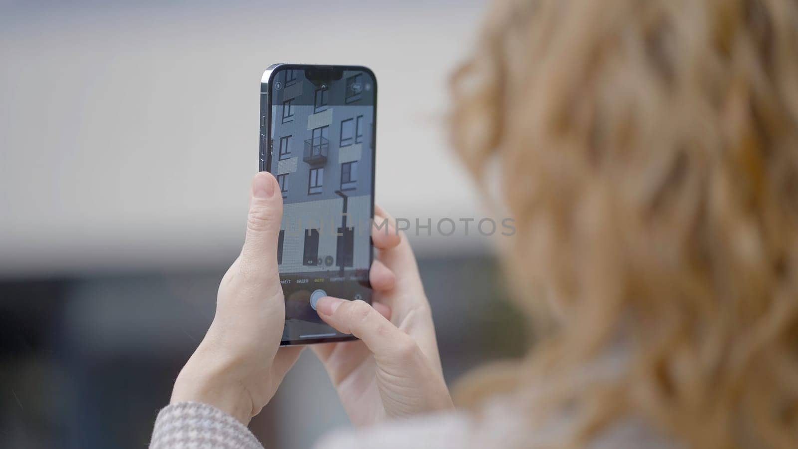 RUSSIA, MOSCOW - SEPTEMBER 27, 2021: Woman takes photos of building on phone. Action. Woman holds phone and takes pictures of building. New improved camera of iPhone 13 by Mediawhalestock