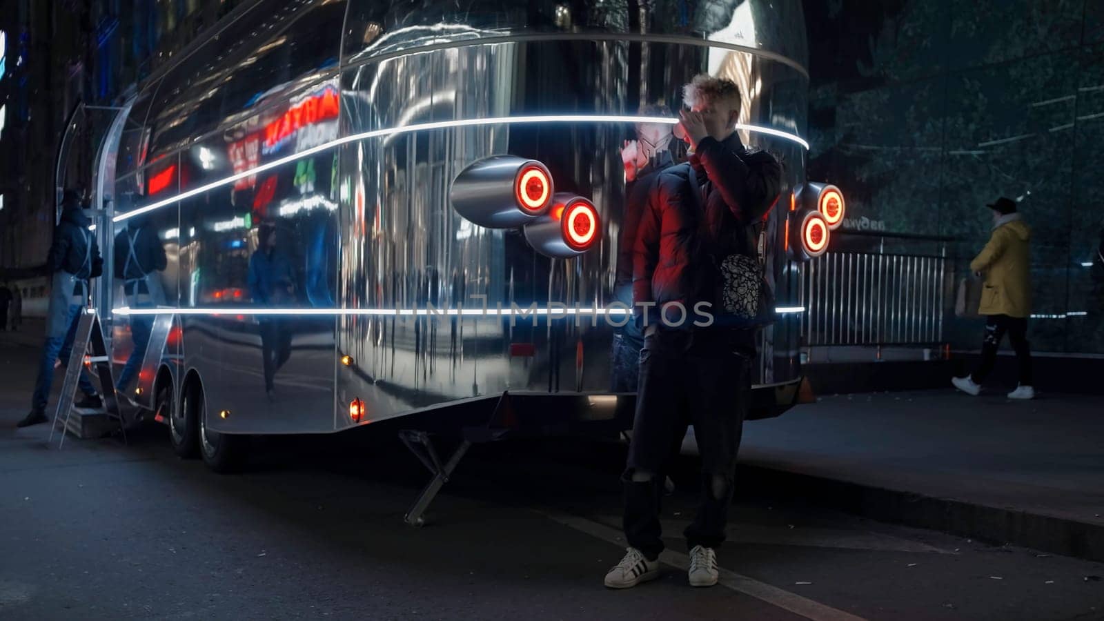 Man standing outdoors in the street near metal futuristic coffee cart shop. Action. Man with a cup of coffee in the evening
