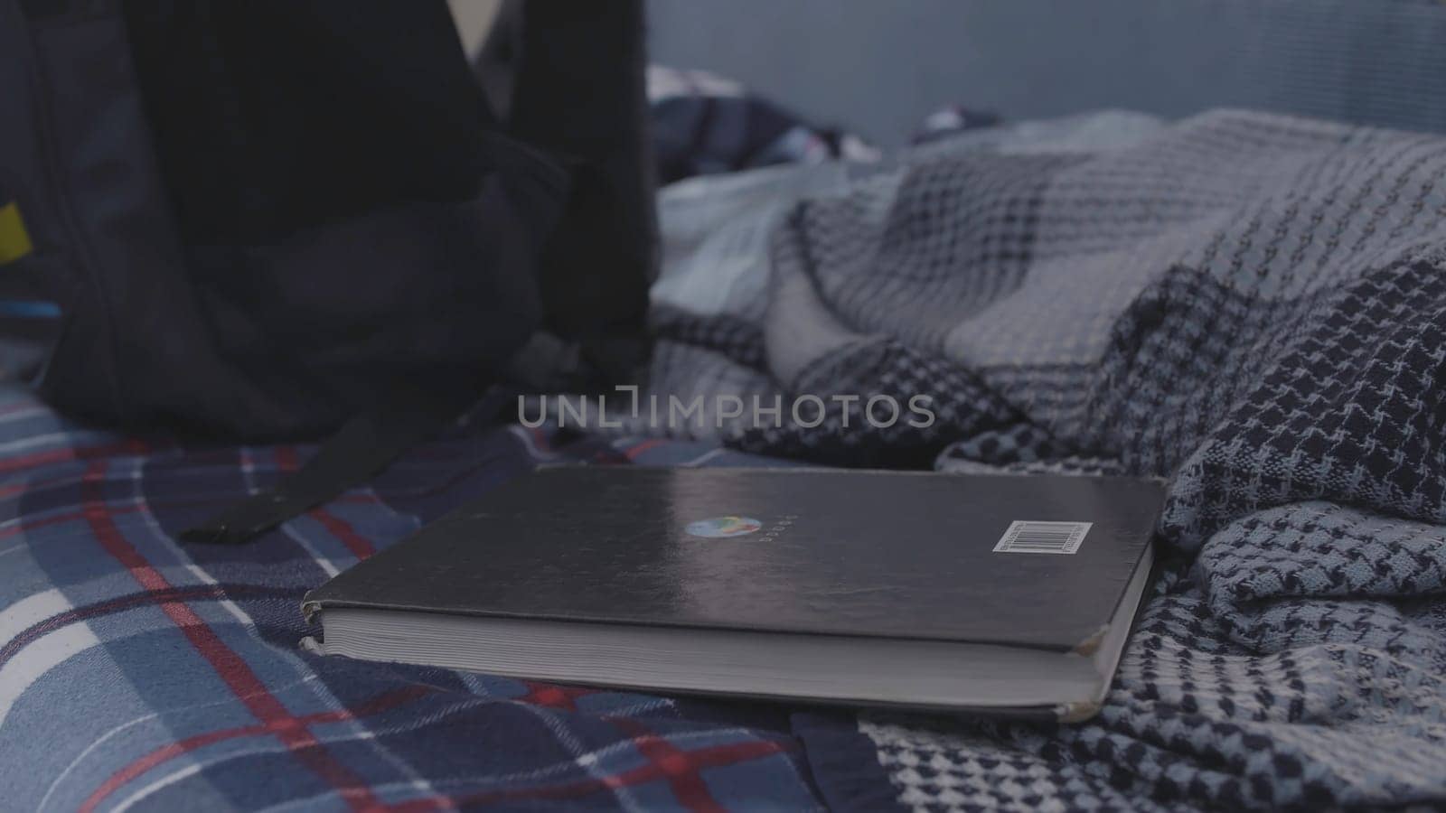 Side view of a boy taking a school textbook from the bed and putting it into the backpack. Young boy getting his backpack ready for school, education concept.