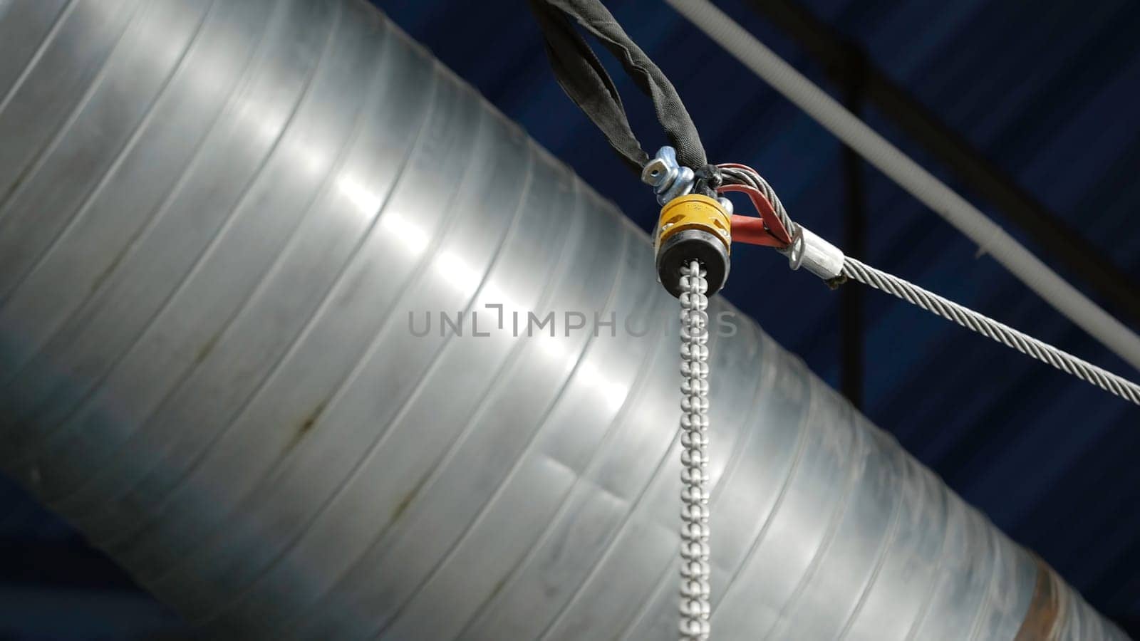 Bottom view of the suspension metal cable on th background of the ceiling and ventilation pipe. Technological details of the industrial room.