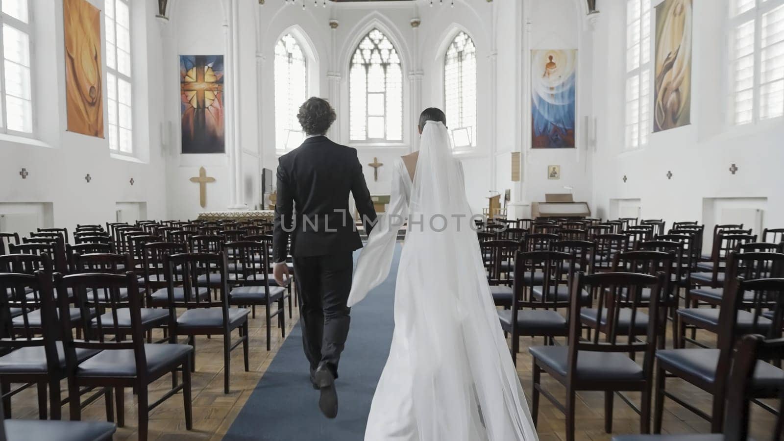 Beautiful newlyweds walking down aisle. Action. Rear view of couple of newlyweds in church. Newlyweds walk down aisle at wedding rehearsal.