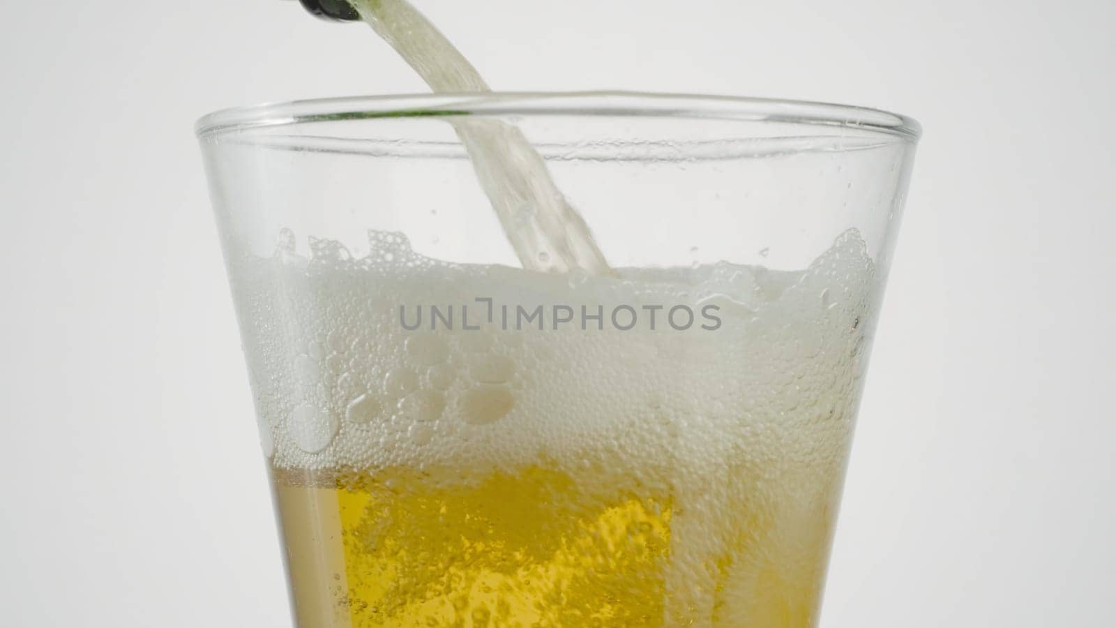 Close-up of beer being poured into clear glass. Action. Beer is poured into transparent glass on white isolated background. Beer is poured into glass.