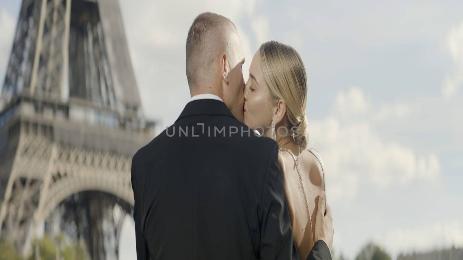 A kissing European couple. Action. A young beautiful blonde woman with her man kissing on the background of the Eiffel Tower. by Mediawhalestock