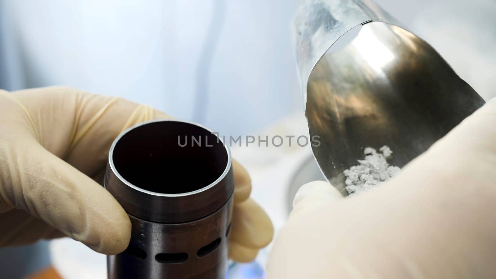 Close up of hands in medical gloves putting chemical powder from chemical scoop to small metal container at laboratory. Hands putting white reagent into chemical receptacle, science conceept