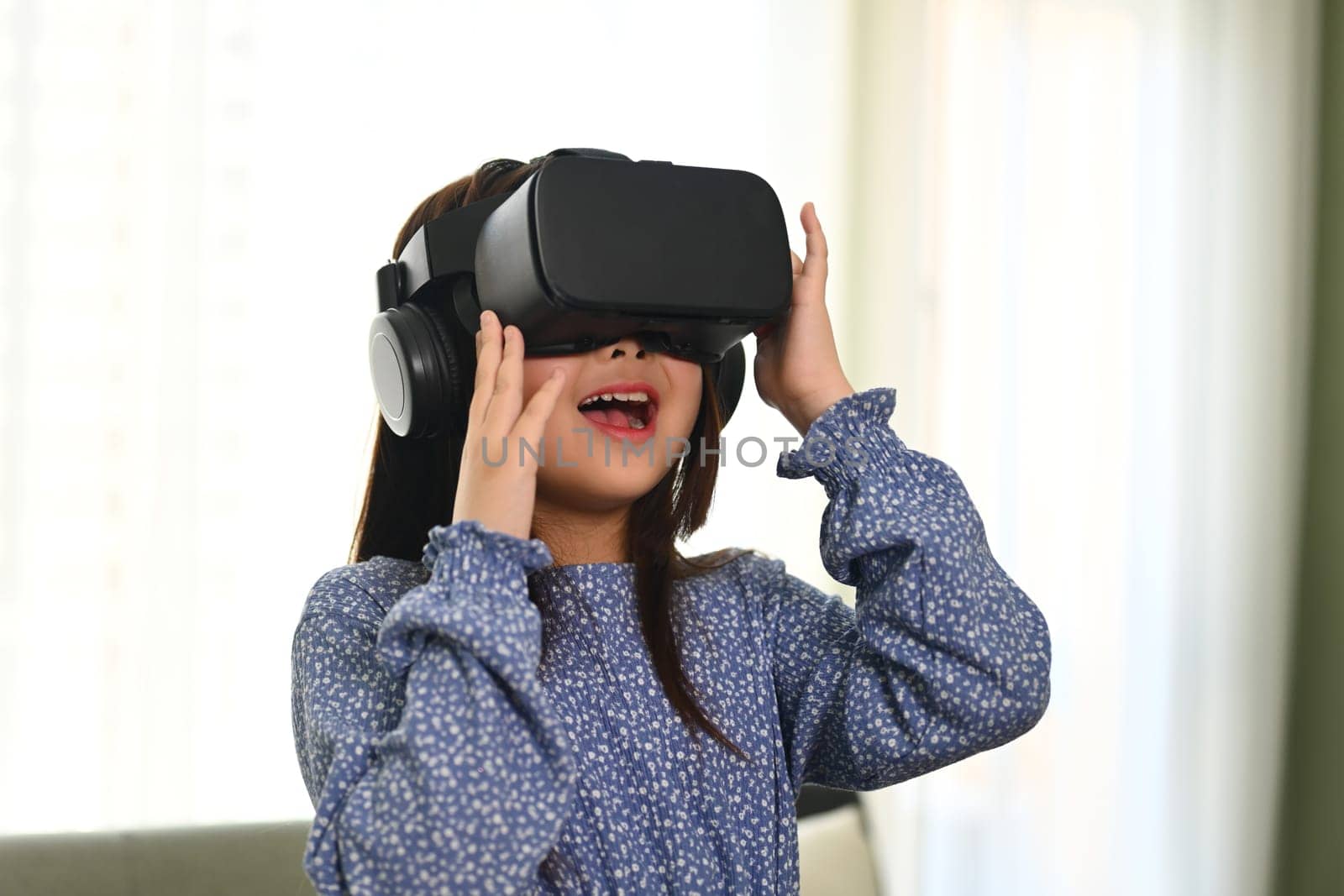 Excited little girl playing games, experiencing via VR headset. Innovative technologies concept.