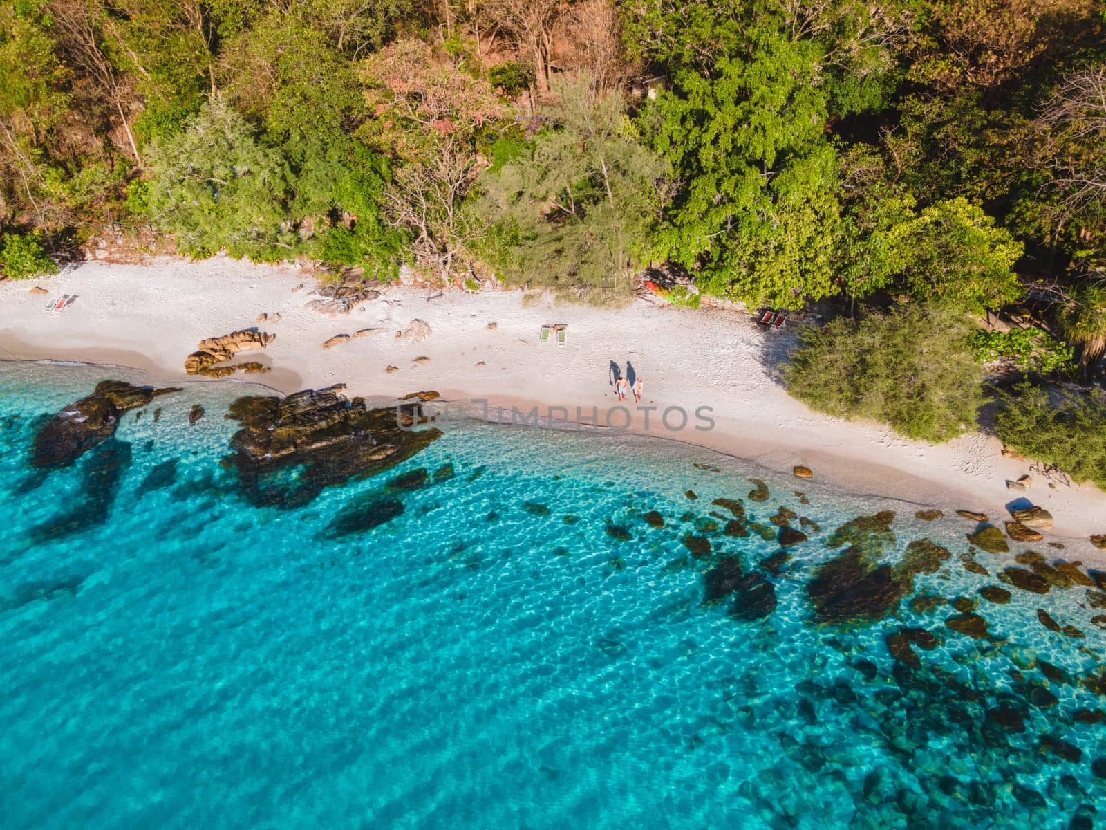 Koh Samet Island Thailand, aerial drone view from above at a couple of men and woman on the beach of Samed Island in Thailand with a turqouse colored ocean and a white tropical beach on a sunny day