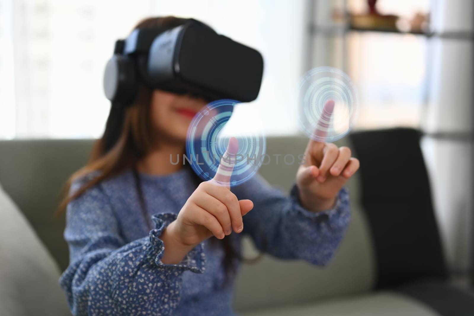 Little girl wearing VR headset and touching virtual button interacting with digital interface.