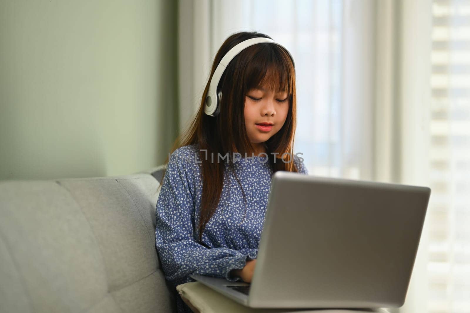 Concentrated Asian girl in headphone watching online lesson on laptop computer at home.