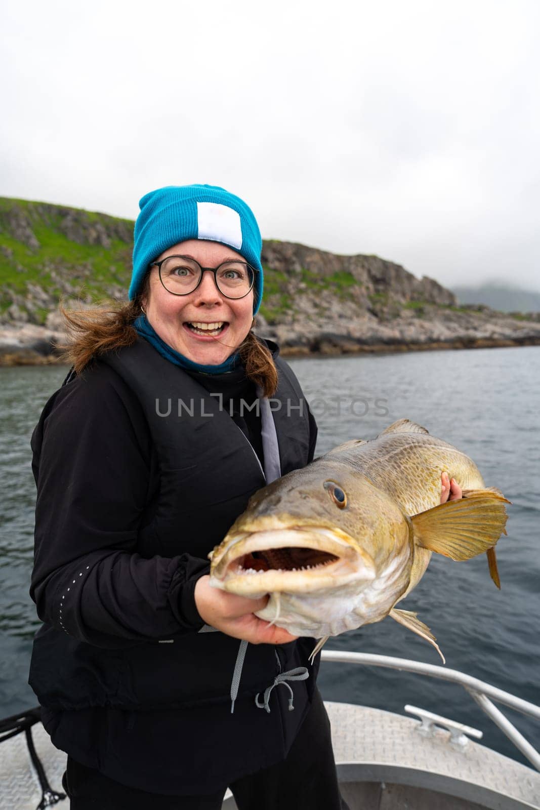 Happy young woman holding big arctic cod. Norway happy fishing. Happy fisherwoman with cod fish in hands. Guided fishing concept. Fishing tourism. Active vacation, open sea, ocean fishing.
