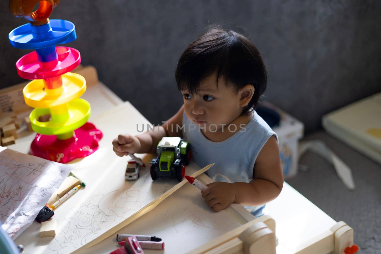 Adorable Boy Sitting On Table Drawing On Paper At Home. 
little toddler boy  draws with Crayons in the paper in the children's room at home. Educational activities for kids.