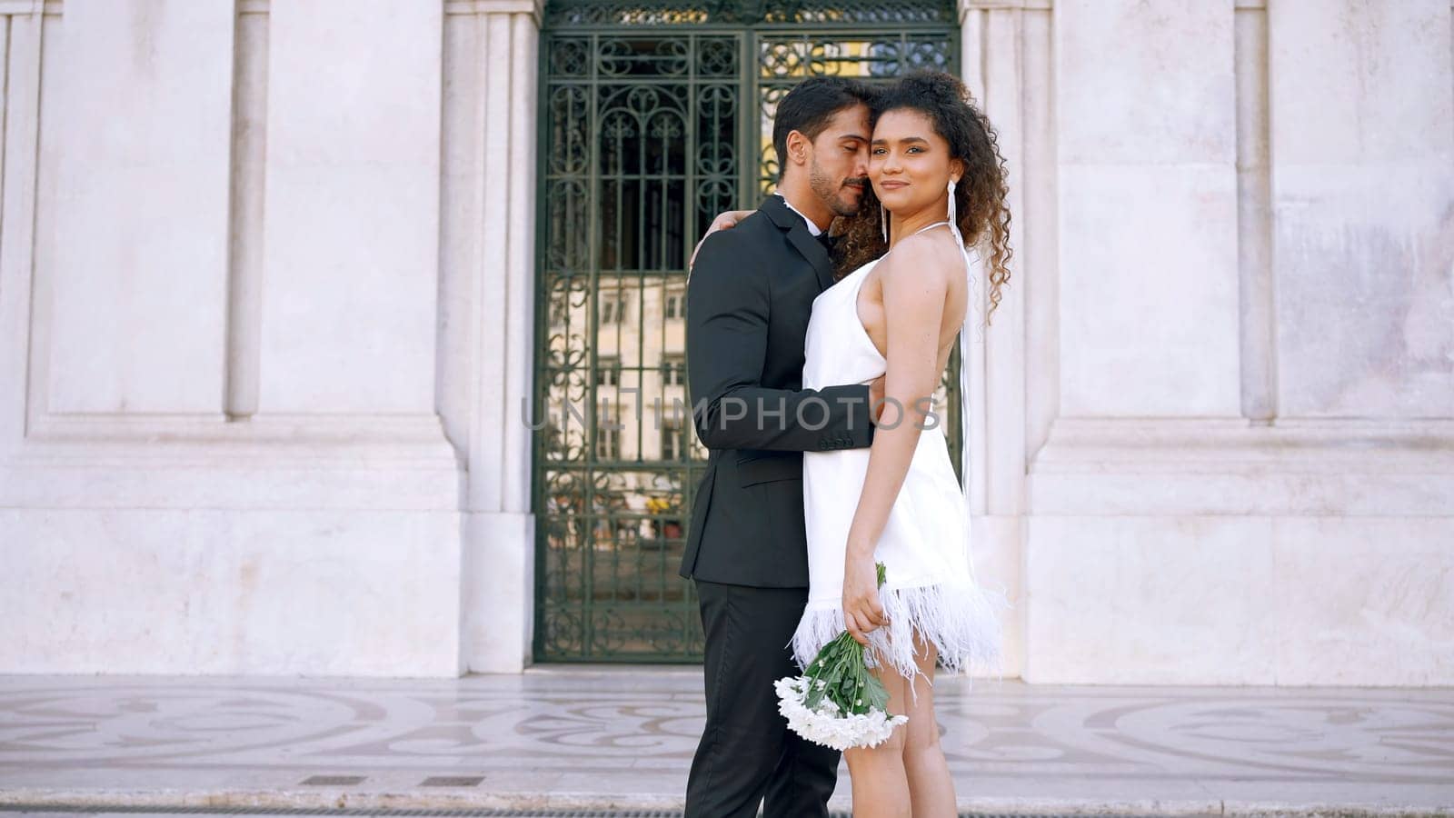 Beautiful couple in outfits happily embracing. Action. Attractive couple in luxurious outfits on street of old town. Gorgeous young couple happily embraces on sunny day.