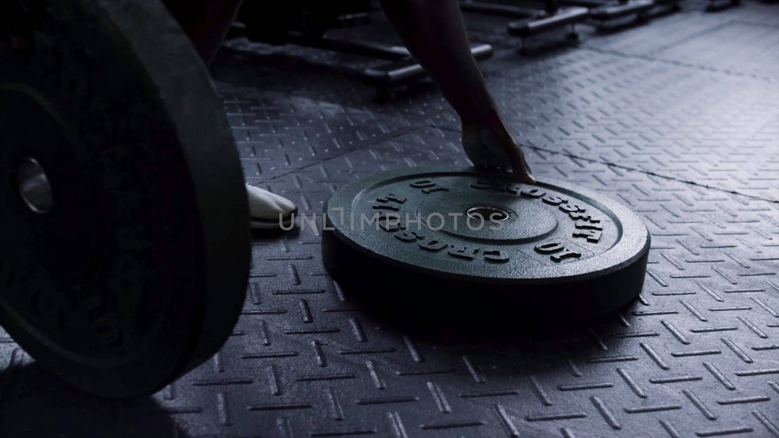 Close up for heavy weight plates on the gym floor ready to be used by a man for strength workout. Man taking fitness exercise equipment barbell weights plate from the gym floor, sport concept