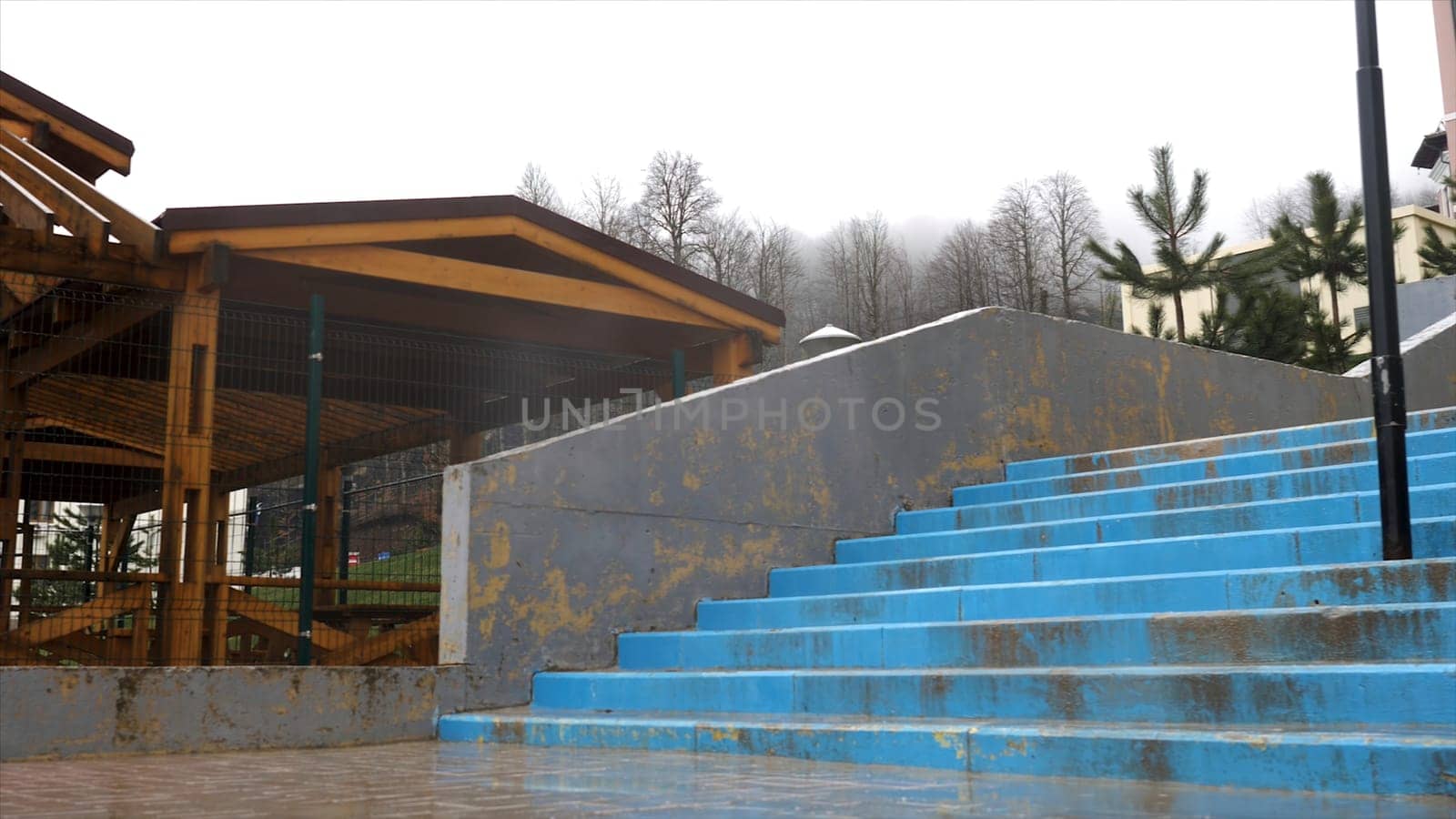 Wooden pavilion in raining season located near concrete stairs on grey heavy sky background. Covered gazebo under the rain in late autumn.