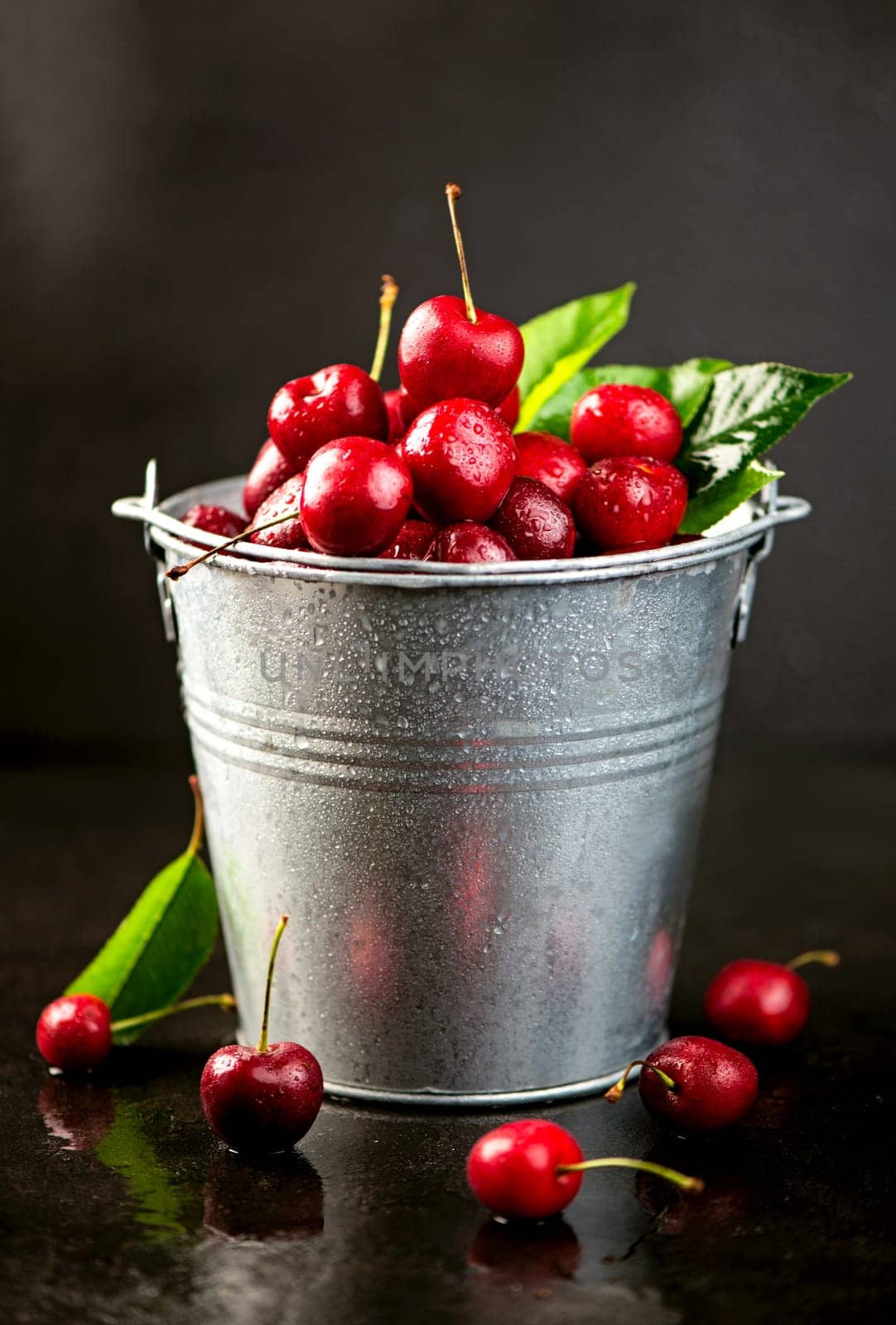 Preparing cherries for jam. Ripe sweet cherry berry with leaves in a bucket on a black wooden board by aprilphoto