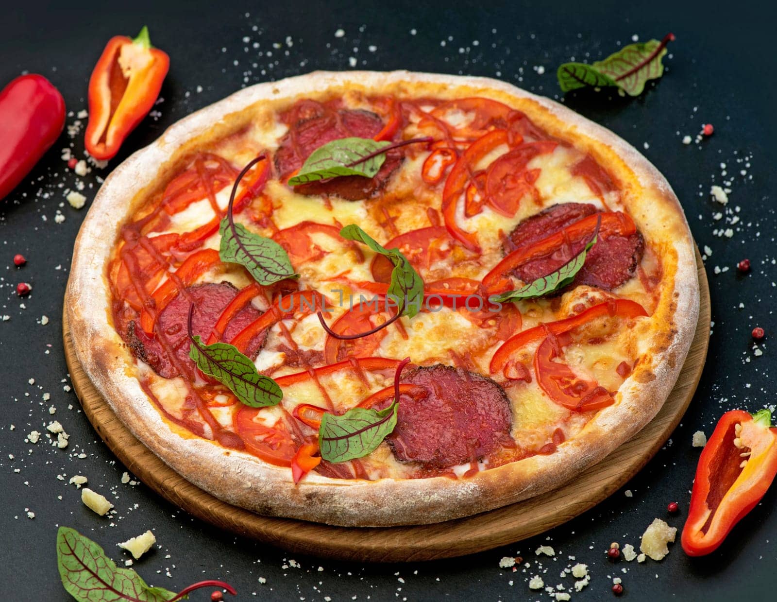 Spicy pizza with cheese, salami, bell pepper and basil on a black background. Delicious pizza with meat and cheese by aprilphoto