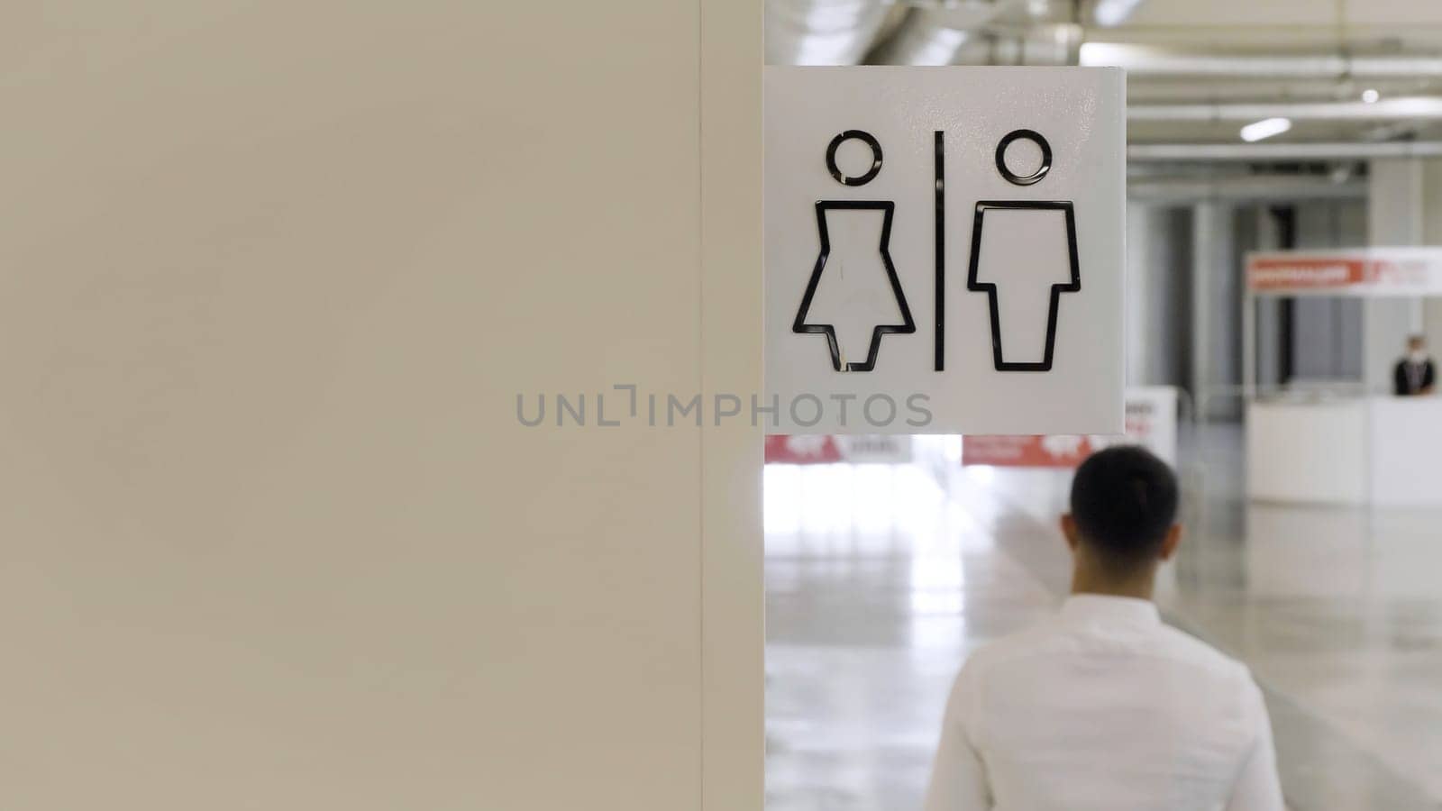 Men and women bathrooms sign at the shopping center. HDR. Rear view of a man in white shirt walking by the beige wall with male and female symbols of a public toilet