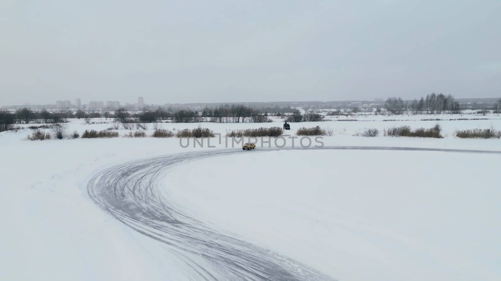 Aerial view of a driving car at snowy track at winter. Clip. One car driving through ice covered lake
