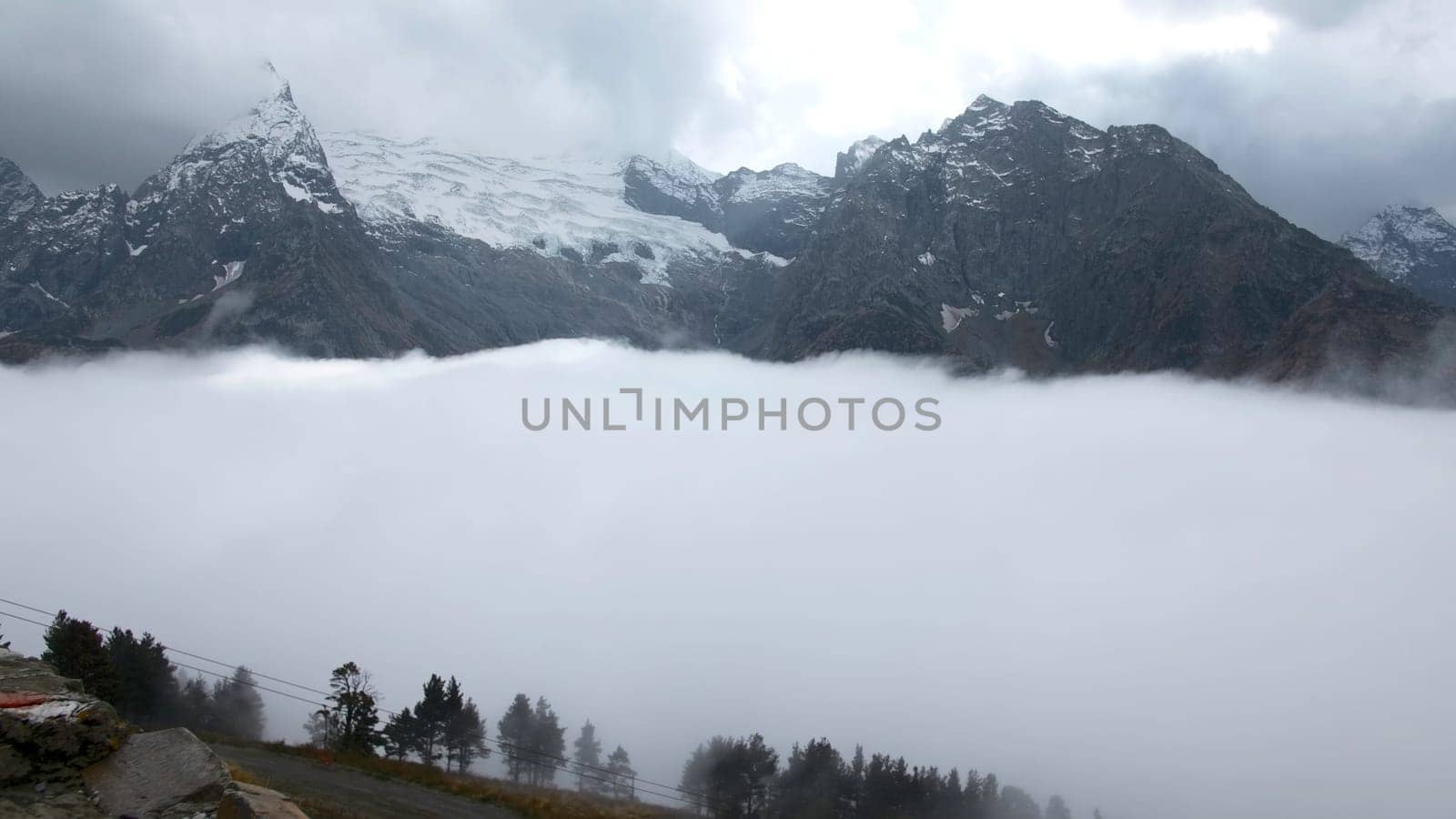 Fly over majestic mountain peaks and a fog. Creative. Valley covered by clouds and mountains on the background