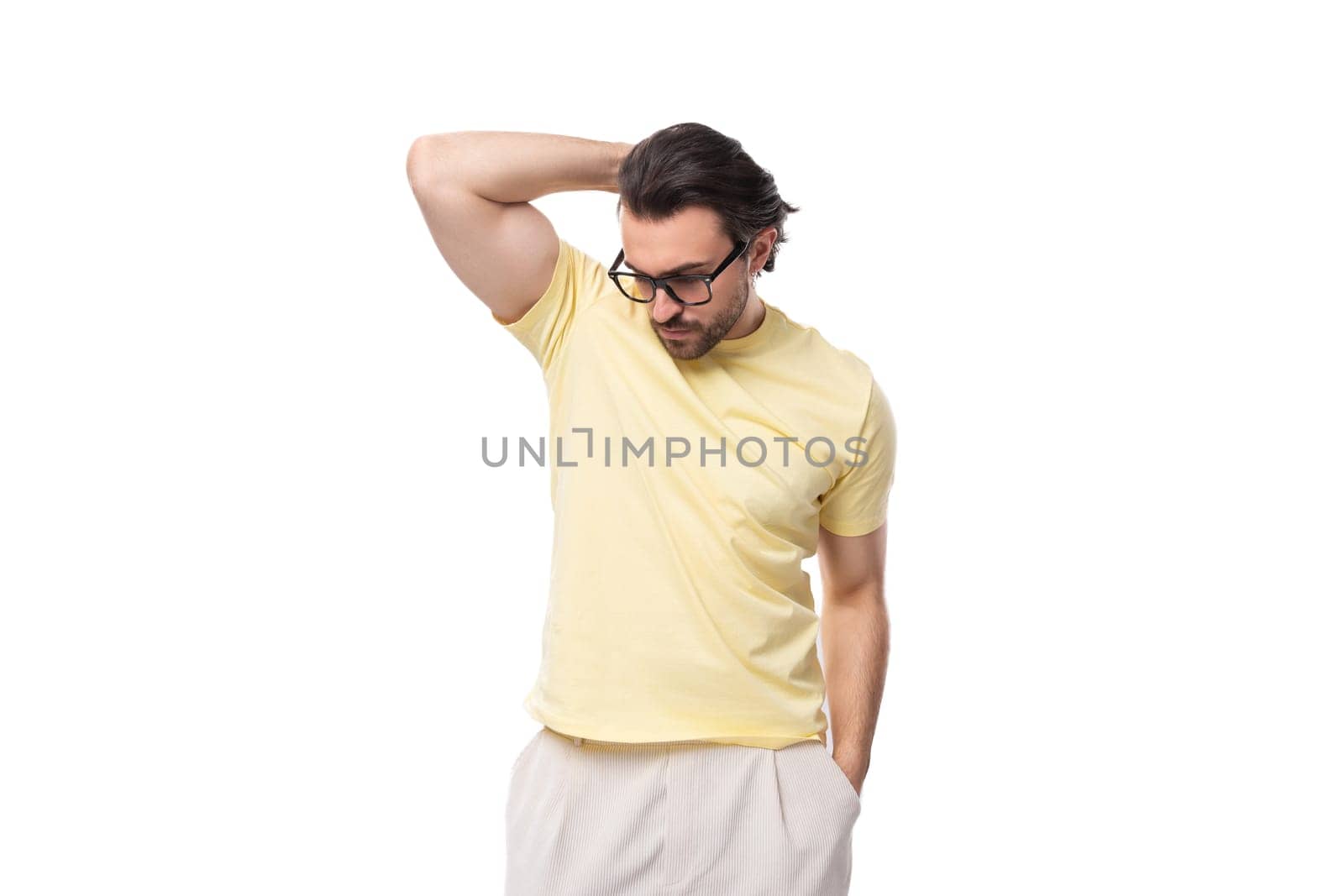 fashionable young successful European guy with stubble and mustache dressed in a light yellow T-shirt put on glasses.