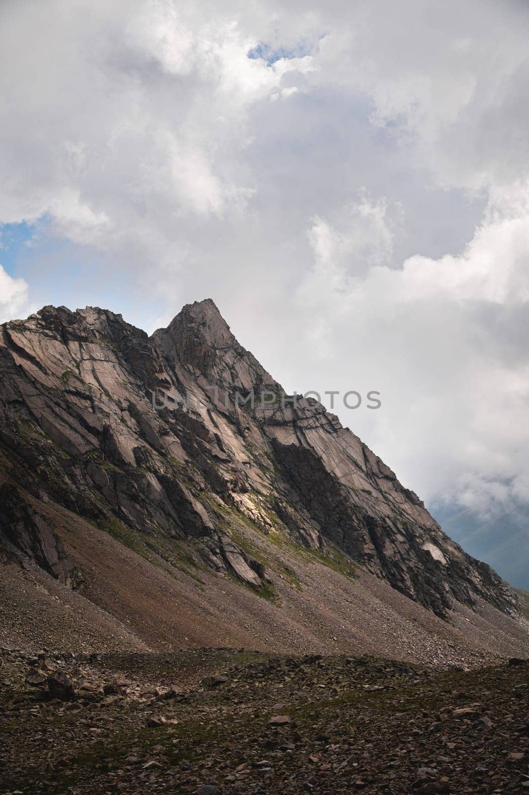 Close-up of a mountain wall at daytime against the backdrop of cumulus clouds.