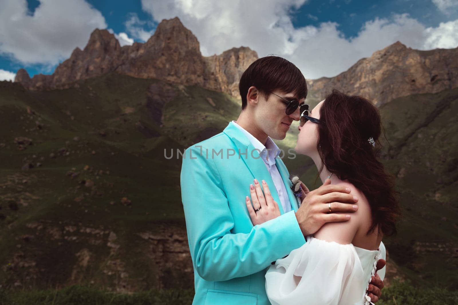 Beautiful wedding couple laughs and plans to kiss against the backdrop of mountains and cloudy sky. Portrait of happy newlyweds.