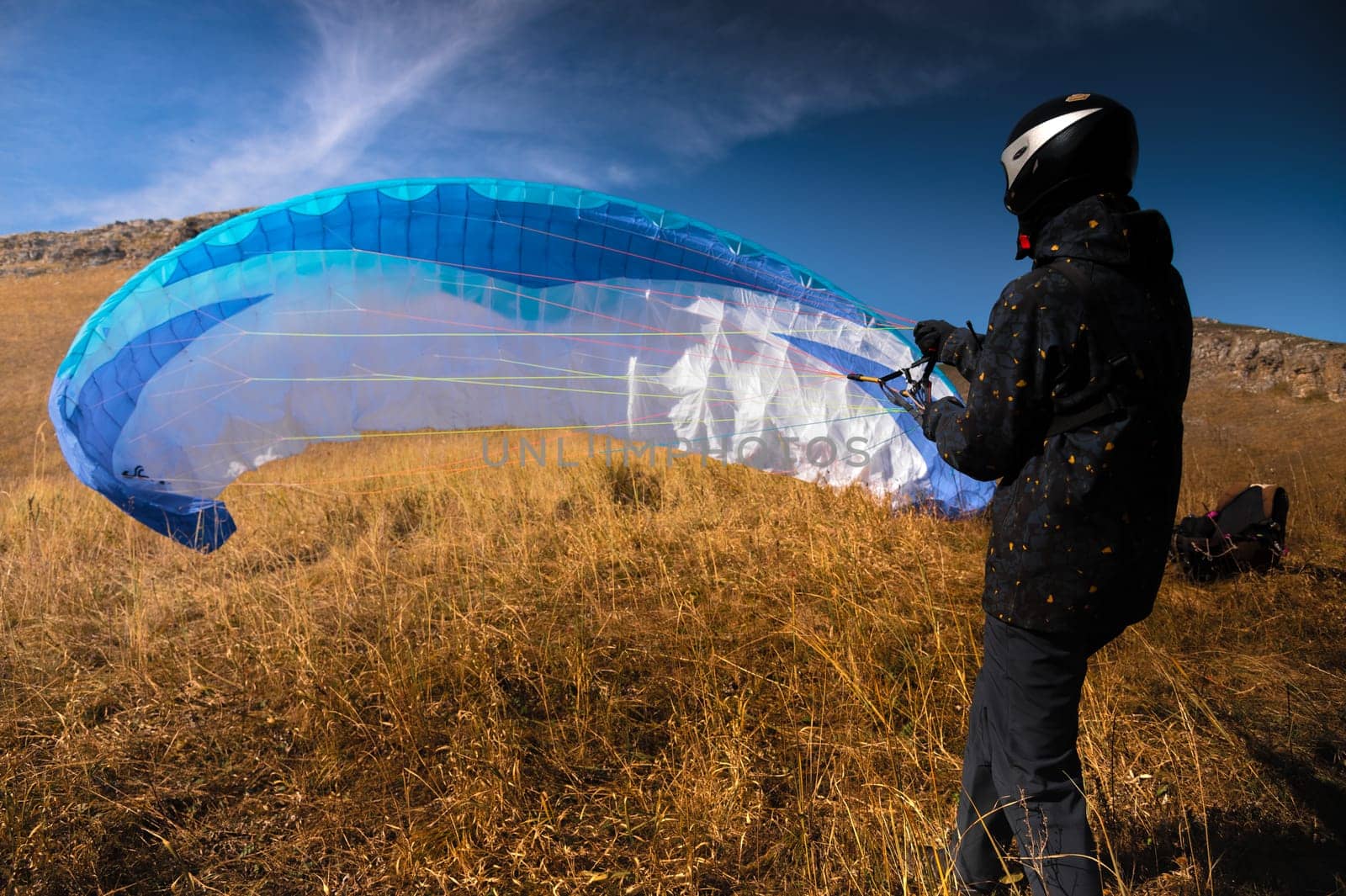 paraglider lands or rises on the yellow grass on a sunny day. A man after or before a paragliding flight. Glider with parachute, wide angle rear view by yanik88