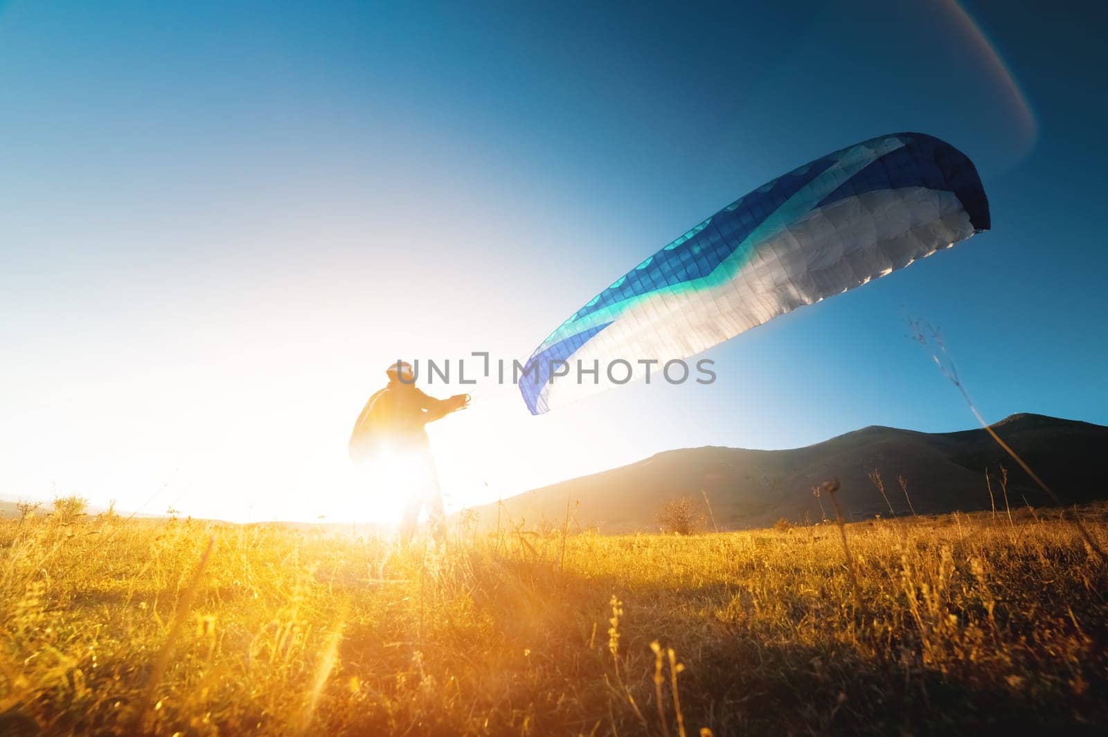 Launching a speedwing from a mountain. A paraglider is preparing to take off from a mountain, running along the yellow autumn grass against the sun by yanik88