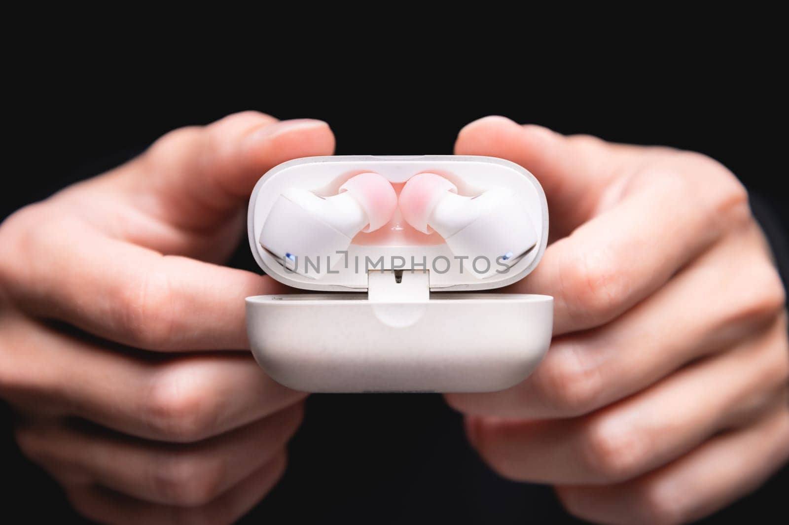 wireless headphones in a white case on a background, a hand with an open lid shows the device from the inside.