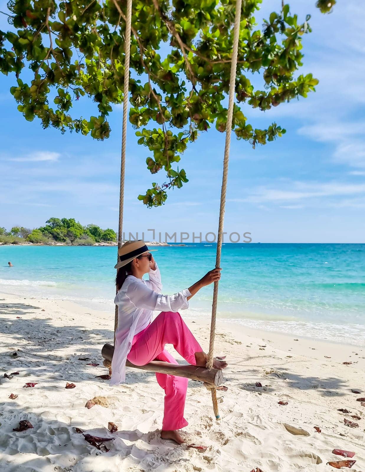 Asian woman on a swing at the beach of Koh Samet Island Rayong Thailand, the white tropical beach of Samed Island with a turqouse colored ocean on a sunny afternoon