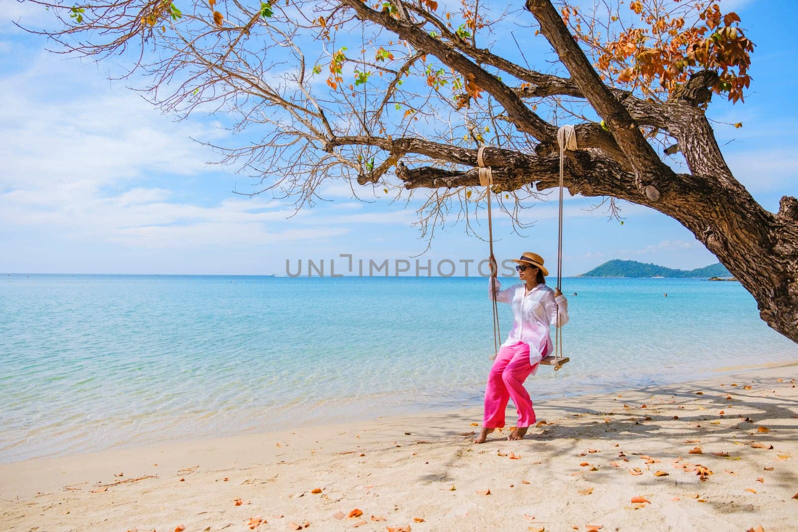 Asian woman on a swing at the beach of Koh Samet Island Rayong Thailand, the white tropical beach of Samed Island with a turqouse colored ocean on a sunny afternoon