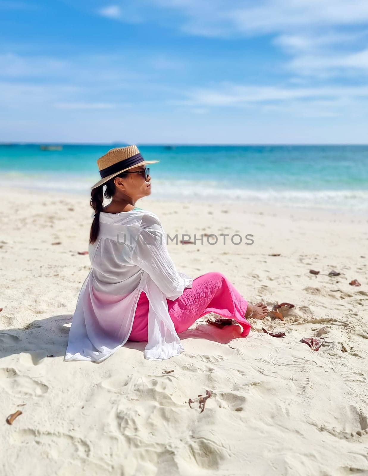 Asian woman sitting on the beach of Koh Samet Island Rayong Thailand, the white tropical beach of Samed Island with a turqouse colored ocean