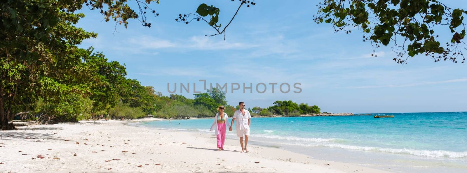 A couple of men and woman walking on the beach of Koh Samet Island Rayong Thailand, the white tropical beach of Samed Island with a turqouse colored ocean