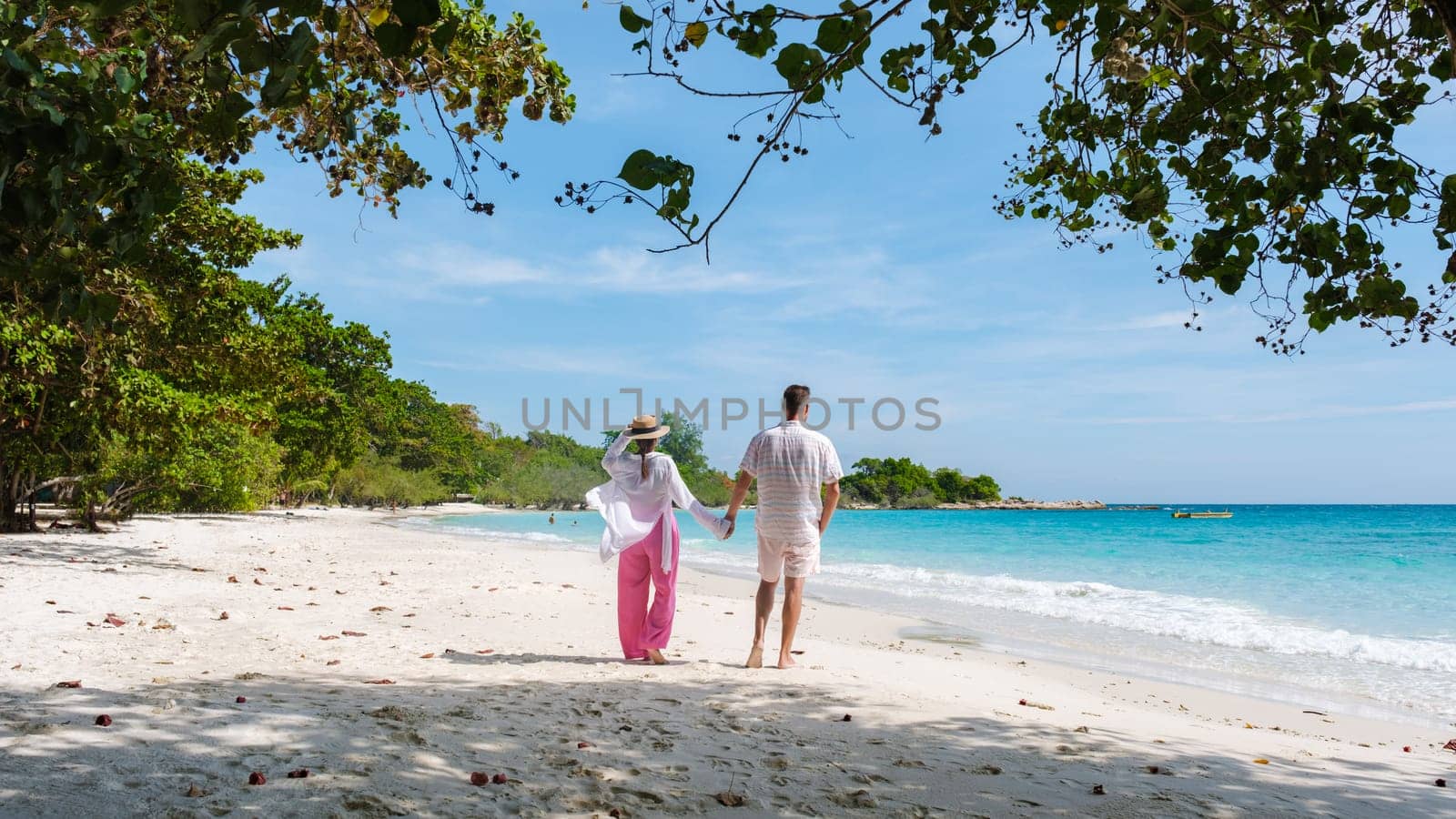 A couple of men and woman walking on the beach of Koh Samet Island Rayong Thailand, the white tropical beach of Samed Island with a turqouse colored ocean
