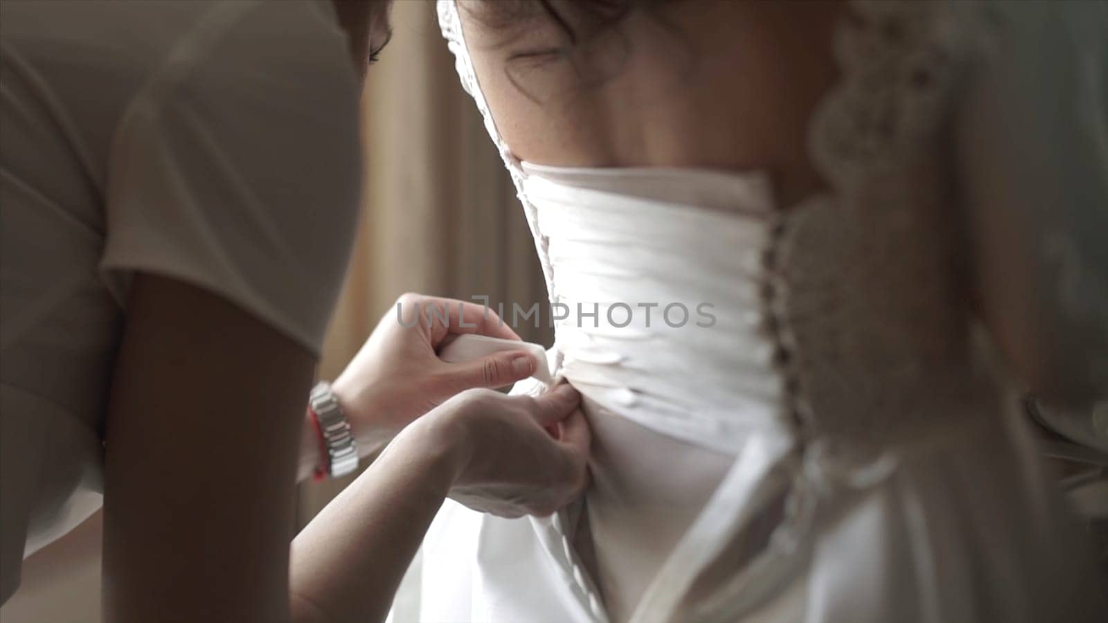 Stylish beautiful bridesmaids helping gorgeous brunette bride in white dress get ready for wedding, morning preparations, woman putting on dress. Mom and bridesmaid, help to dress a wedding dress HD