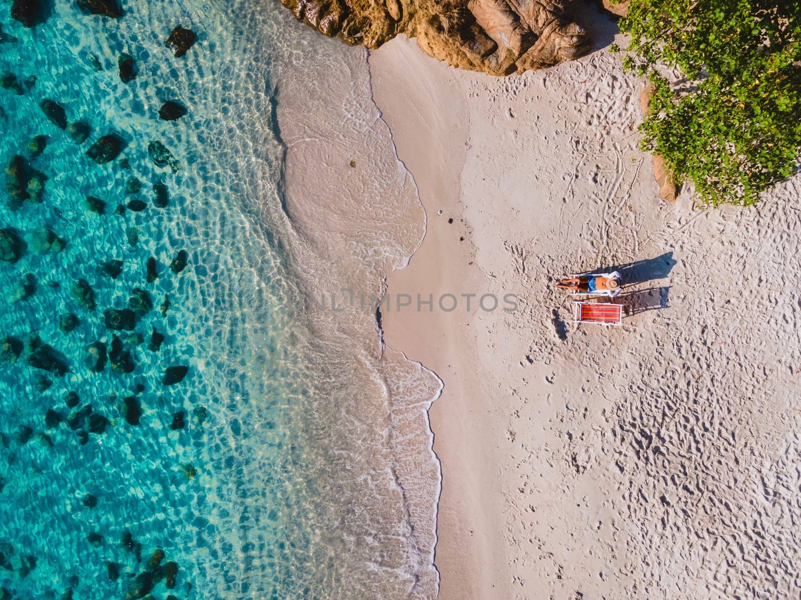 aerial drone view from above at a couple of men and woman on the beach of Samed Island in Thailand, with a turqouse colored ocean and a white tropical beach Koh Samt Thailand