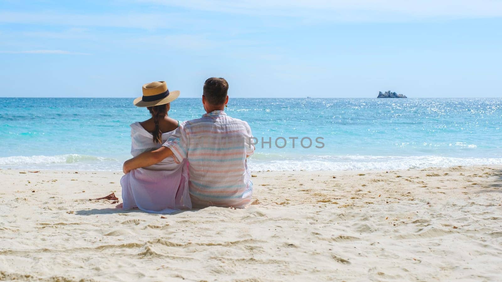 A couple of men and woman sitting on the beach looking out over the ocean of Koh Samet Island Rayong Thailand.