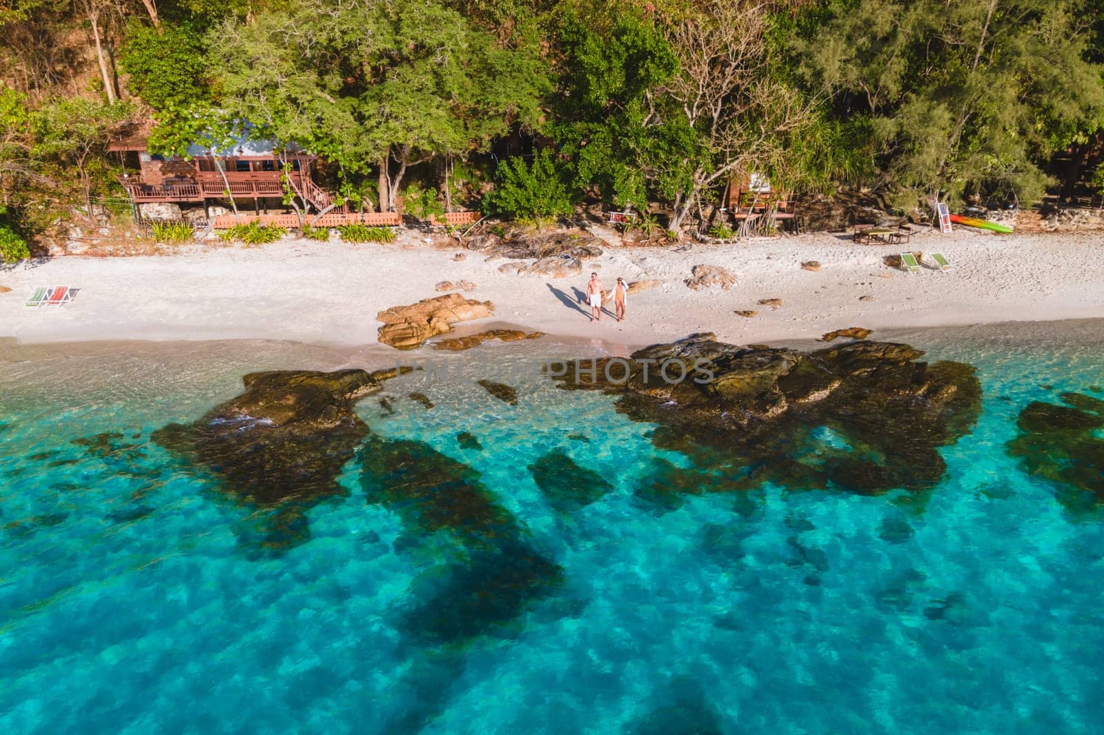 Koh Samet Island Thailand, aerial drone view from above at a couple of men and woman on the beach of Samed Island in Thailand with a turqouse colored ocean and a white tropical beach