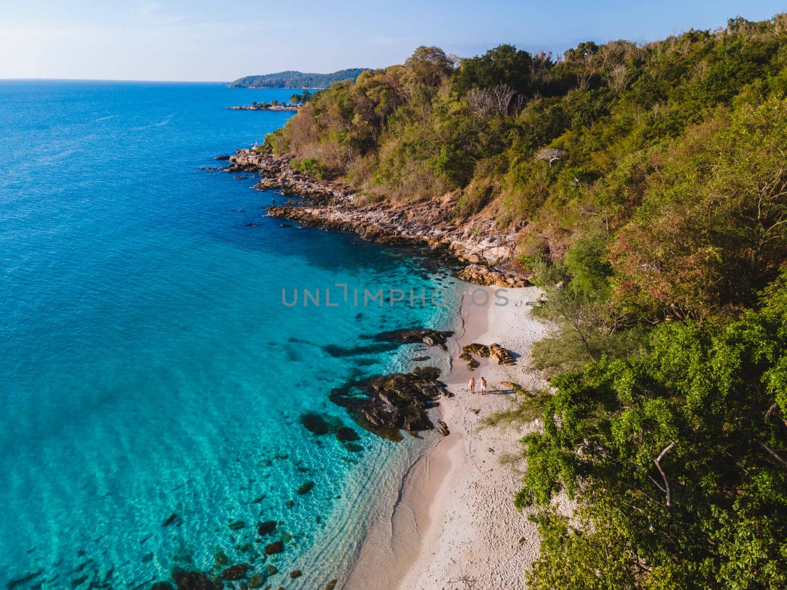 aerial drone view from above at a couple of men and woman on the beach of Samed Island in Thailand, with a turqouse colored ocean and a white tropical beach Koh Samt Thailand