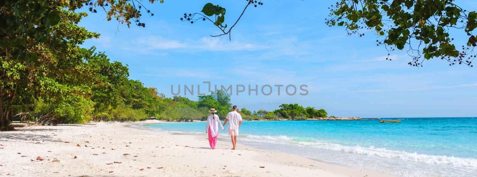 A couple of men and woman walking on the beach of Koh Samet Island Thailand, the white tropical beach of Samed Island with a turqouse colored ocean, Asian Thai woman and European men on the beach