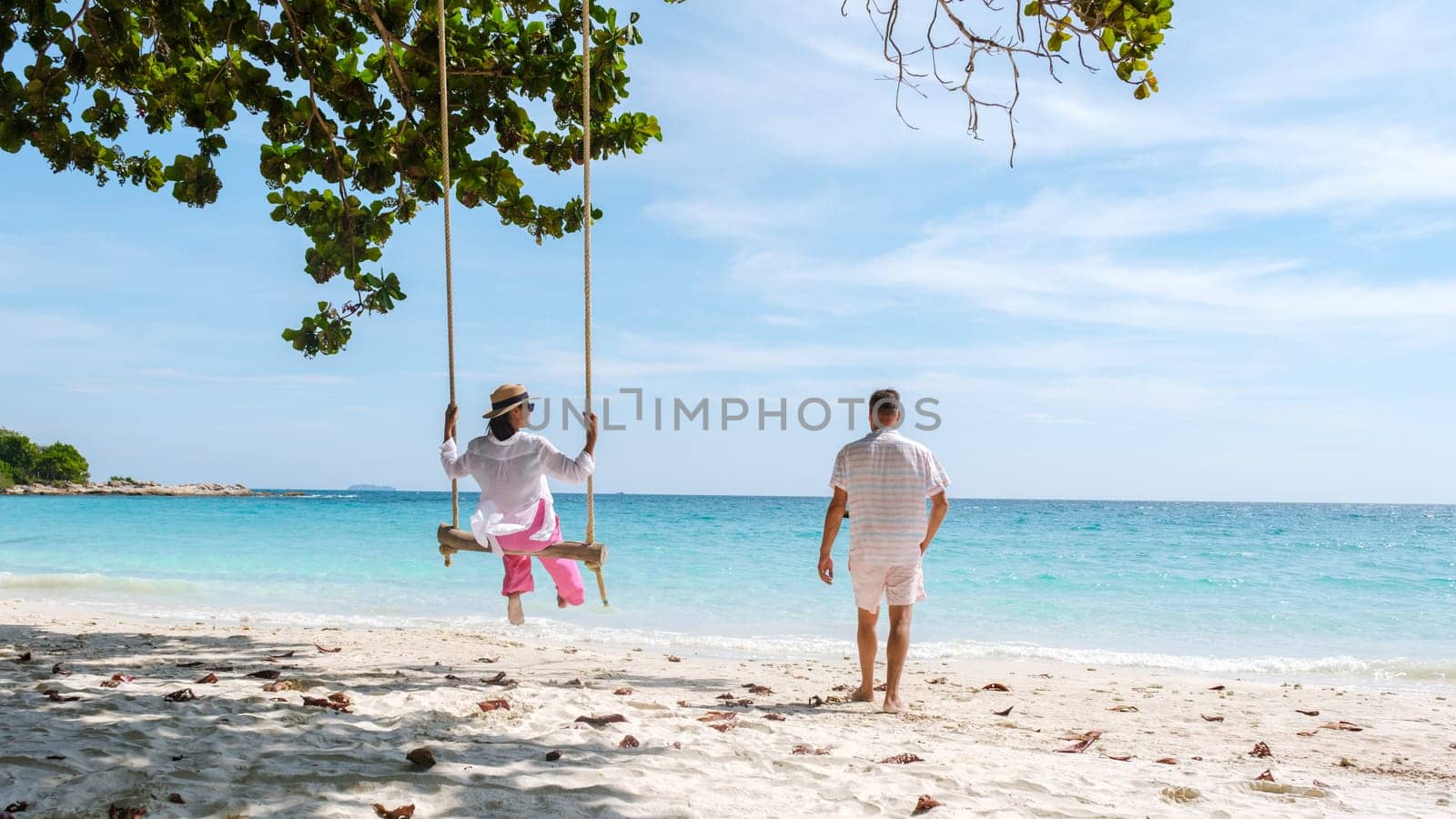 A couple of men and women at a swing on the beach of Koh Samet Island Rayong Thailand, the white tropical beach of Samed Island with a turqouse colored ocean.