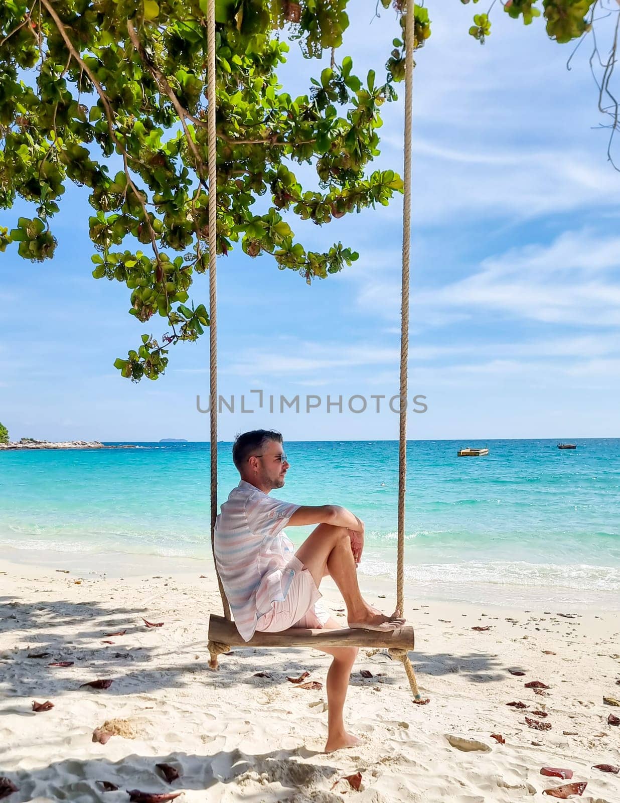 Men sitting on a swing at the beach of Koh Samet Island Rayong Thailand, the white tropical beach of Samed Island with a turqouse colored ocean