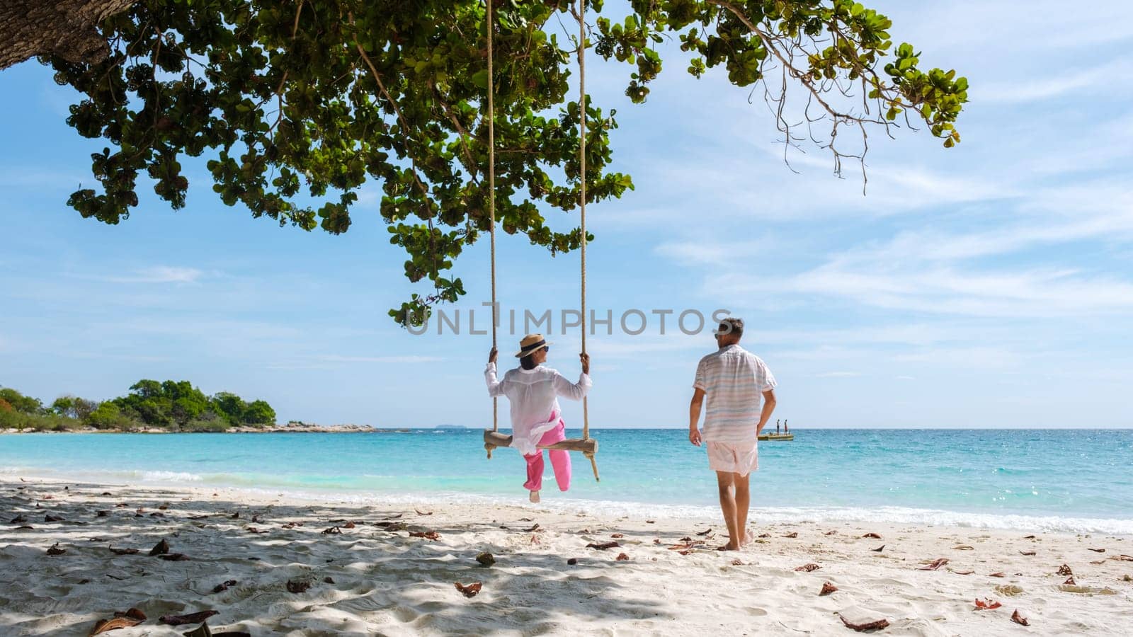 A couple of men and women at a swing on the beach of Koh Samet Island Rayong Thailand, the white tropical beach of Samed Island with a turqouse colored ocean. Asian woman and European men on vacation