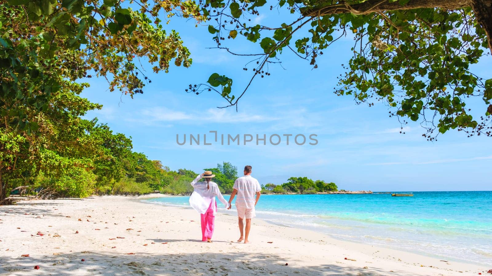 A couple of men and woman walking on the beach of Koh Samet Island Rayong Thailand, the white tropical beach of Samed Island with a turqouse colored ocean