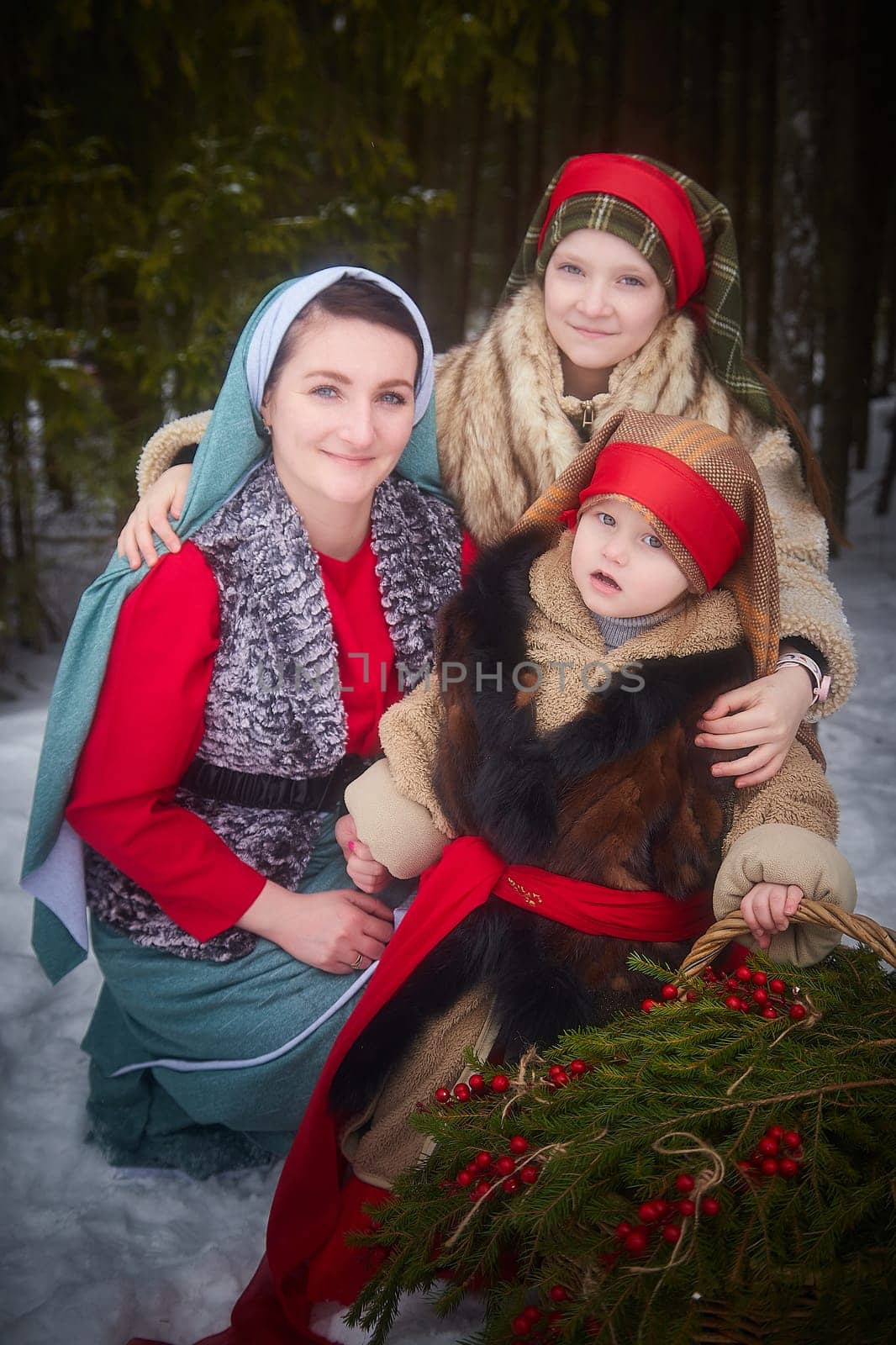 Family with mother, teenage girl, and little daughter dressed in stylized medieval peasant clothing in winter forest. Woman and her daughters pose for fairytale photoshoot in nature on cold day by keleny