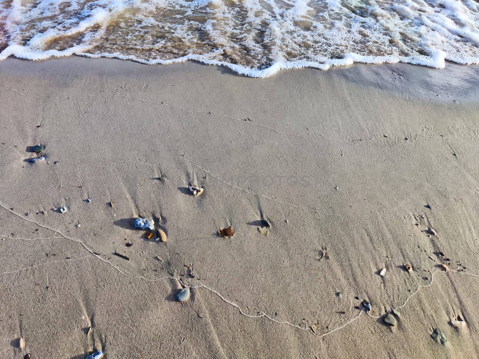 Yellow sand, pebbles and a transparent wave as a background, texture. Abstract pattern, place for text and copy space